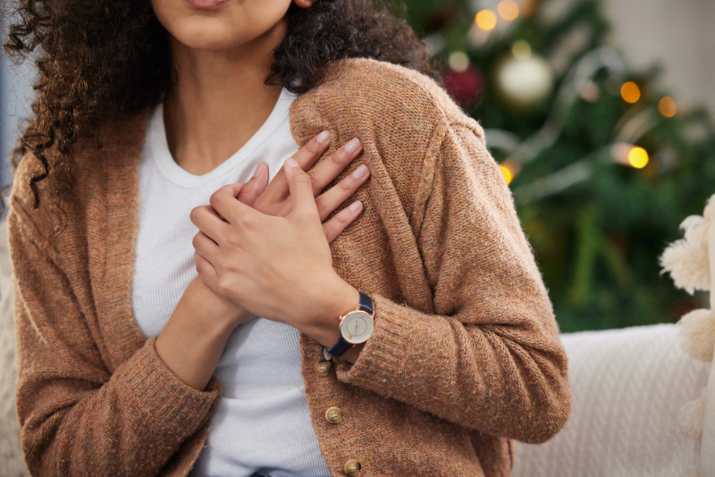 Woman holding her chest with holiday decor in background.