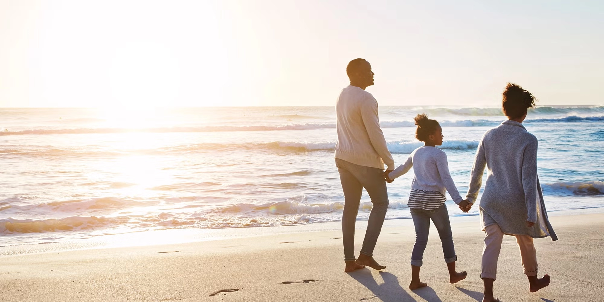 A family of three walks hand in hand with one another on the beach