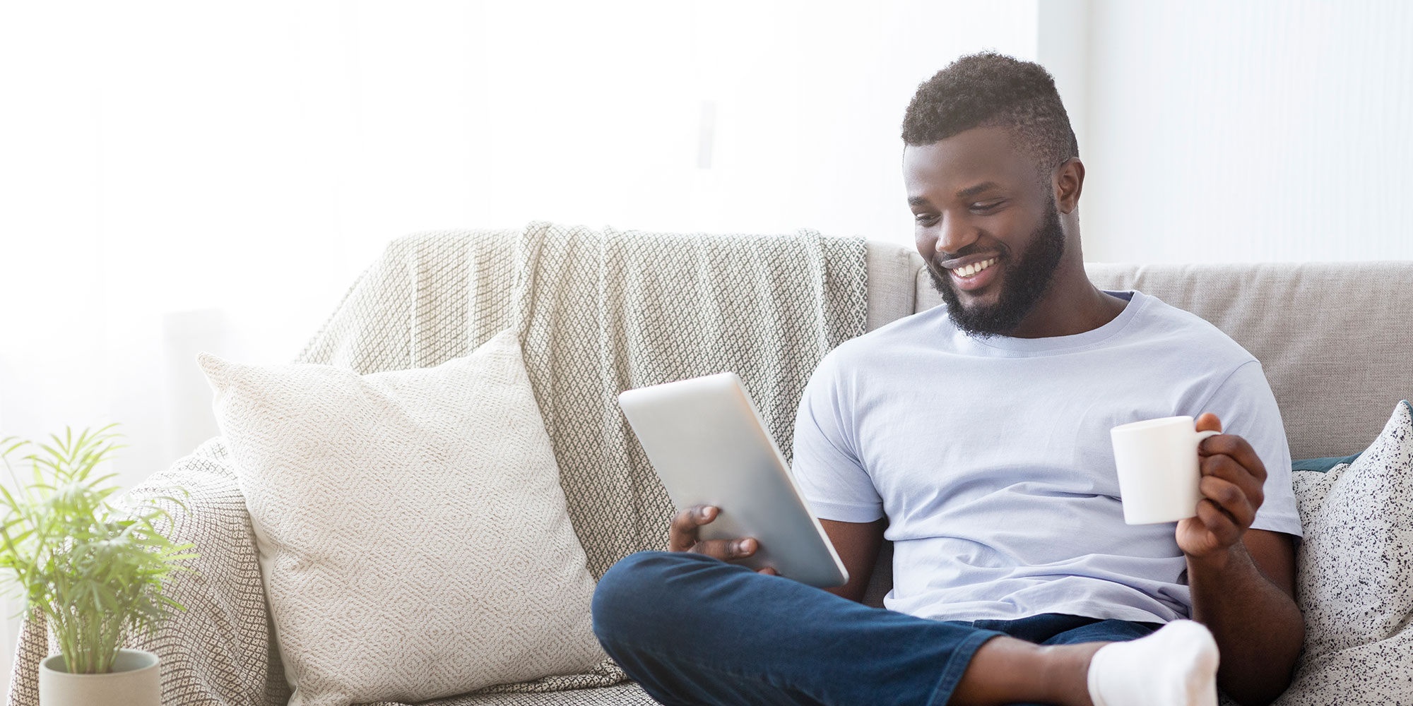 A younger man drinks coffee and reads a newsletter on his tablet