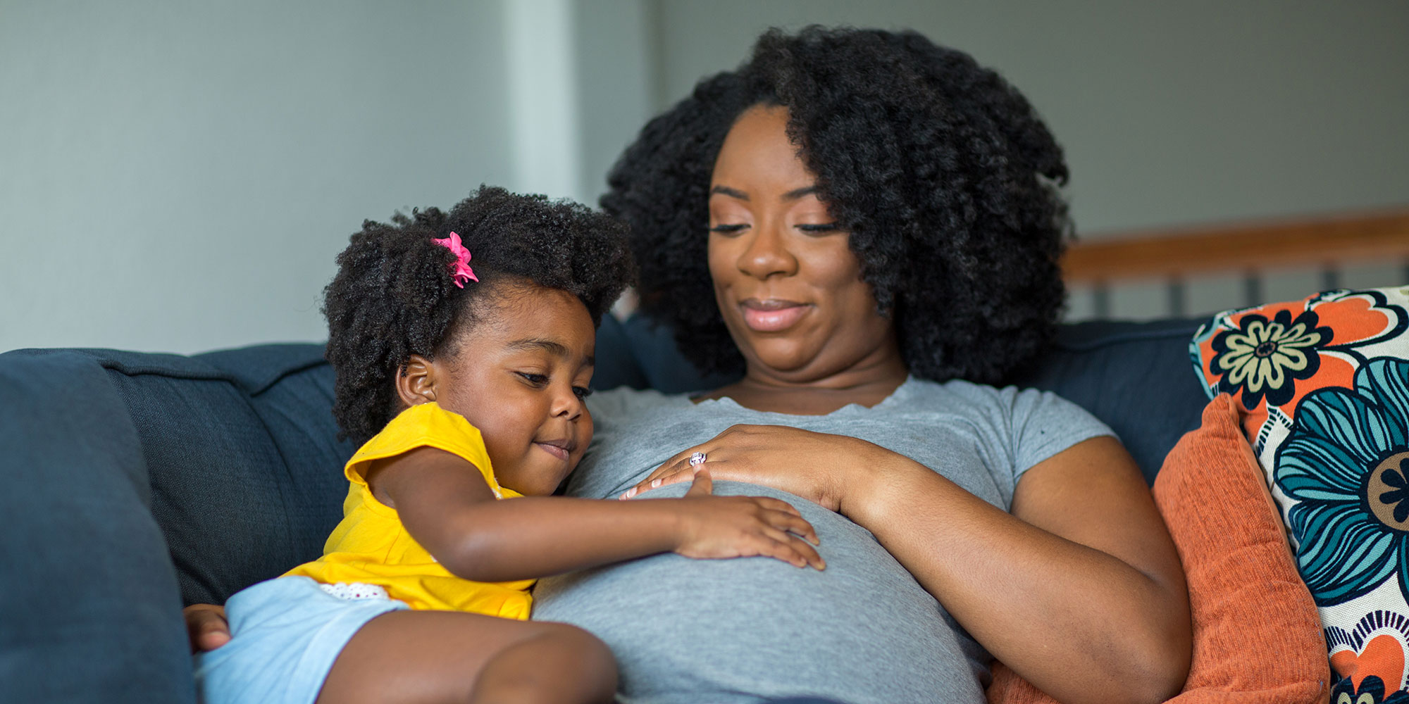 A mother adoringly looks at her daughter, who has her hand on the mother's pregnant belly